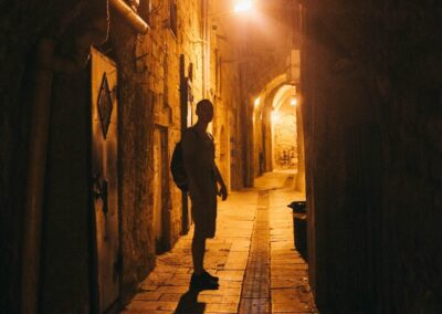 Illuminated Cobbled Street With Light Reflections On Cobblestones In Old Historical City By Night. Dark Blurred Silhouette Of Person Goes In Search Of Adventure In Old Jaffa In Tel Aviv, Israel