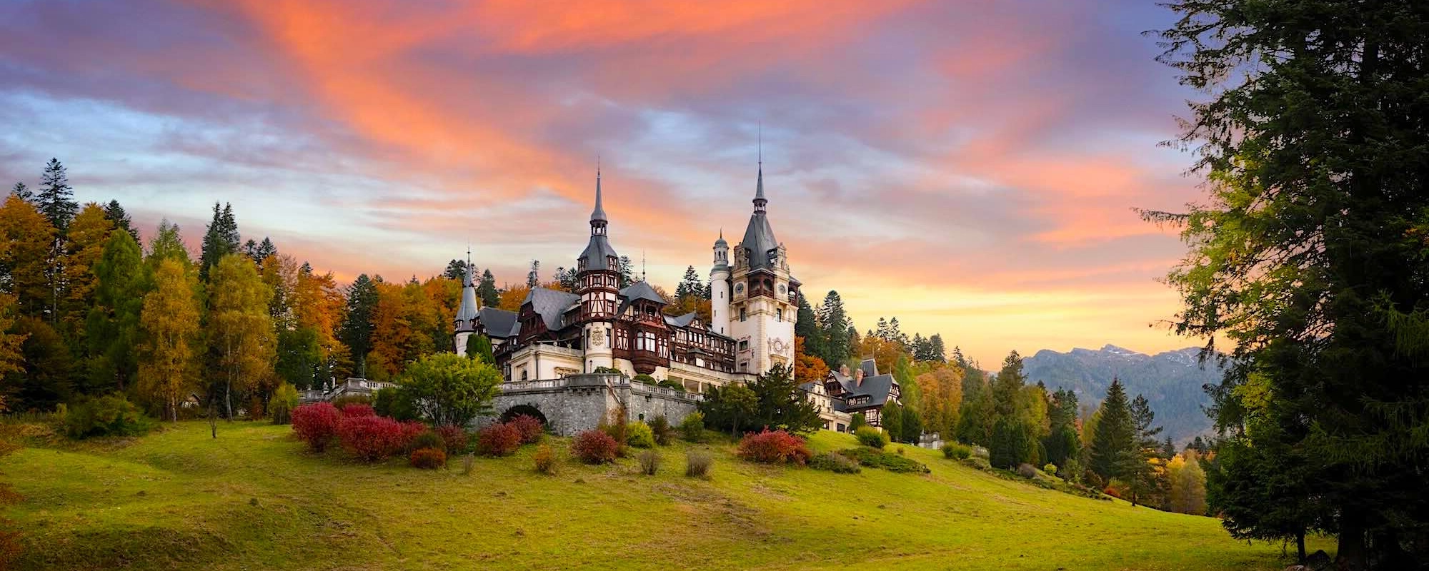 Panorama Of Peles Castle, Romania. Beautiful Famous Royal Castle And Ornamental Garden In Sinaia Landmark Of Carpathian Mountains In Europe At Sunset. Former Home Of The Romanian Royal Family.